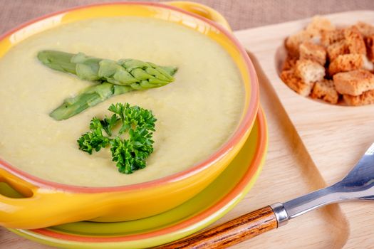 Fresh asparagus creamy soup and ingredients on wooden table on rustic wooden background, selective focus