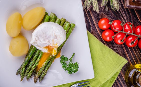 Green asparagus and boiled poached egg on a white plate over a wooden background. selective focus.