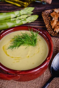 Fresh asparagus creamy soup and ingredients on wooden table on rustic wooden background, selective focus