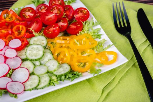 Fresh chopped vegetables on a plate on a wooden table on a rustic wooden background, selective focus
