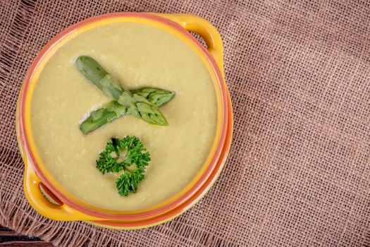 Fresh asparagus creamy soup and ingredients on wooden table on rustic wooden background, selective focus