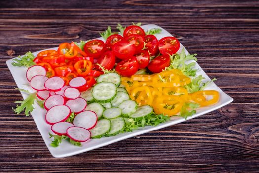 Fresh chopped vegetables on a plate on a wooden table on a rustic wooden background, selective focus