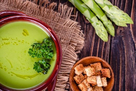 Fresh asparagus creamy soup and ingredients on wooden table on rustic wooden background, selective focus