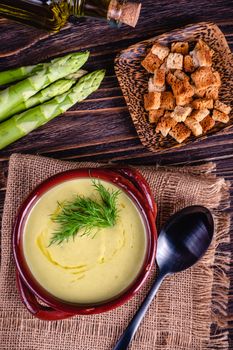 Fresh asparagus creamy soup and ingredients on wooden table on rustic wooden background, selective focus