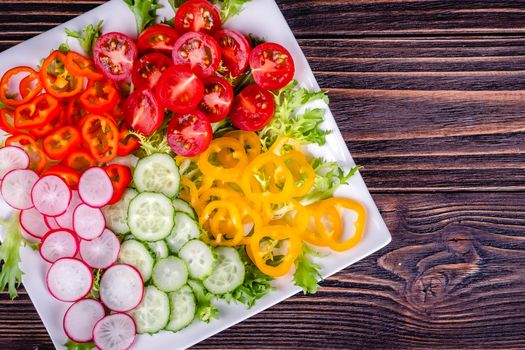 Fresh chopped vegetables on a plate on a wooden table on a rustic wooden background, selective focus