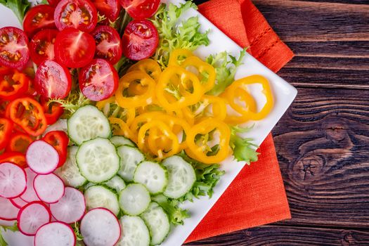 Fresh chopped vegetables on a plate on a wooden table on a rustic wooden background, selective focus