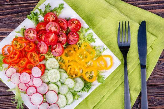 Fresh chopped vegetables on a plate on a wooden table on a rustic wooden background, selective focus