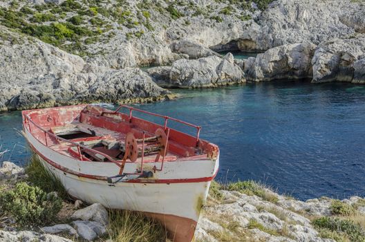 In the small port of Limnionas on the island of Zakynthos we see an old fishing boat perched on top of a cliff and in the background a blue cave on the Ionian sea