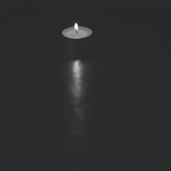 Small lit candle on dark and silver background, black and white, contrast