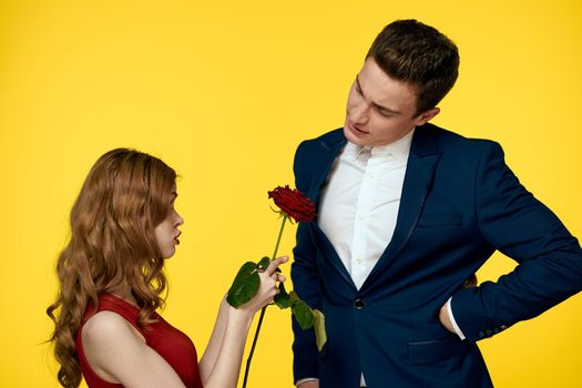 A romantic man hugs a woman in a red dress with a rose in his hand on a yellow background. High quality photo