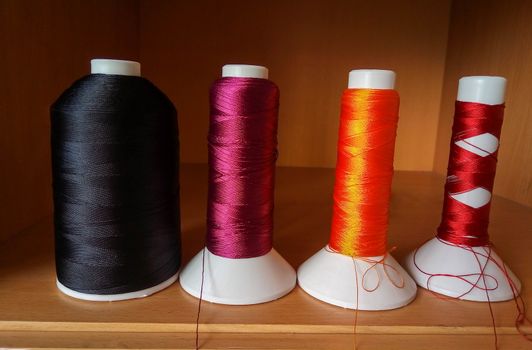 Multicolored sewing threads in bobbins stand on a brown shelf