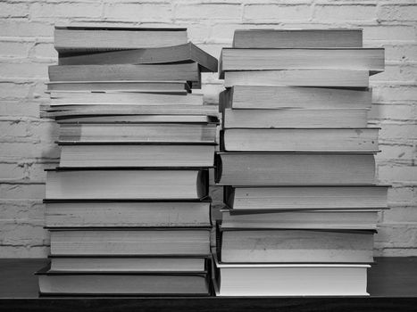 Black and white image of some books stacked on a shelf, light brick background