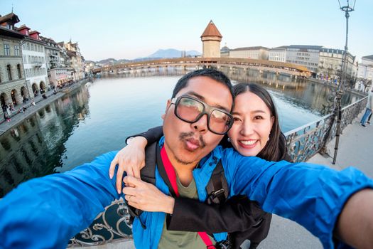 Young Couple Tourists selfie with mobile phone near view of Chapel Bridge Cityscape of Lucerne, Switzerland