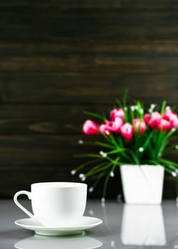 White coffee cup and Artificial flower vase bouquet over table with wood wall background