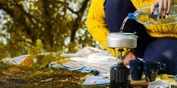 young beautiful girl in a yellow sweater makes coffee in the forest on a gas burner. Making coffee on a primus stove in the autumn forest, step by step. Camping in autumn forest concept