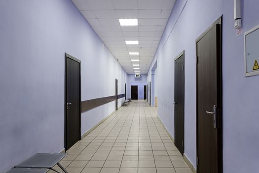 an empty corridor in a modern office building. In a very long corridor with purple walls, there are many brown doors.