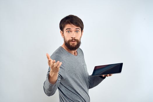 A bearded man with a tablet in his hands a gray jacket technology internet light background. High quality photo