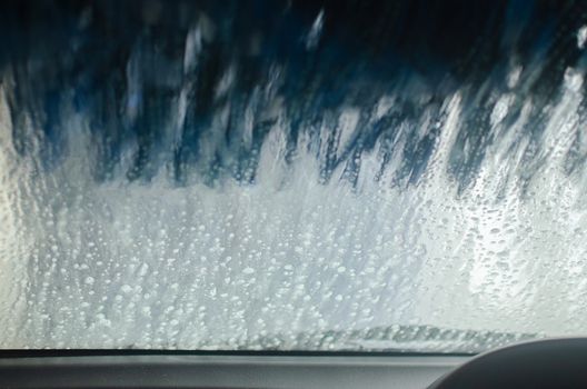 View from inside a car being washed at a car wash from the driver seat. Auto inside carwash from interior. Car windshield cleaning. Automatic conveyorized tunnel vehicle wash.