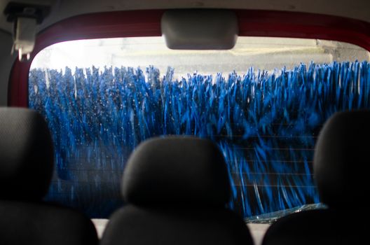 View from inside a car being washed at a car wash from the driver seat. Auto inside carwash from interior. Car windshield cleaning. Automatic conveyorized tunnel vehicle wash.