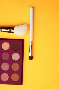 Eyeshadows and makeup brushes on a yellow background top view professional cosmetics. High quality photo