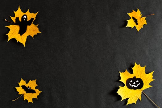 Pumpkin with eyes, Ghost, bats silhouettes made of black paper on yellow maple leaves on a black background. Dark background. Thanksgiving, the concept of Halloween. Flatlay for your design. copyspace