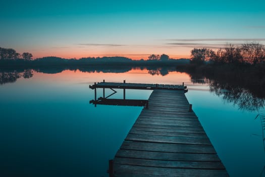 Wooden pier and a view of a calm lake after sunset, autumn landscape