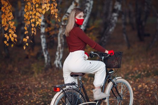 Young woman riding bicycle in red gloves and face mask at autumn park.