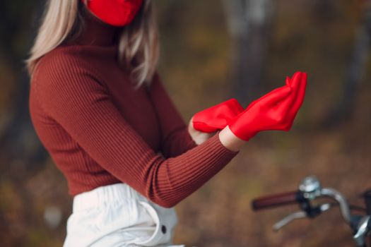 Young woman riding bicycle in red gloves and face mask at autumn park.