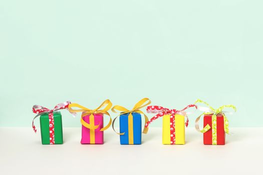 Row with five colorful gift boxes on a pastel background. Copy space. Front view.