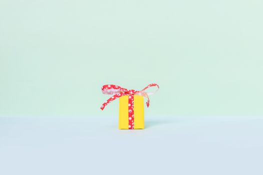 Yellow gift box with red ribbon on a pastel background. Copy space. Front view.