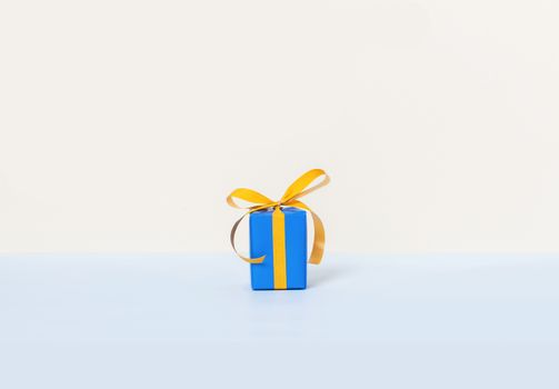 Blue gift box with yellow ribbon on a pastel background. Copy space. Front view.