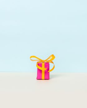 Magenta gift box with yellow ribbon on a pastel background. Copy space. Front view.