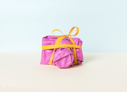 Photo camera wrapped in magenta gift paper and yellow ribbon on a pastel background. Front view.