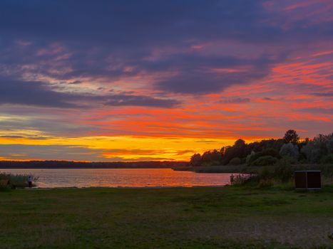 Panoramic view of evening sunset lake with green trees, mist and tranquil reflection. Estonia, Harku. Sunset over lake