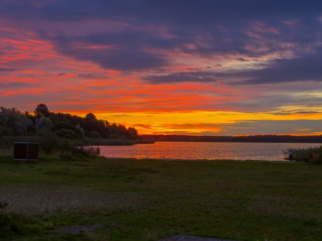 Panoramic view of evening sunset lake with green trees, mist and tranquil reflection. Estonia, Harku. Sunset over lake