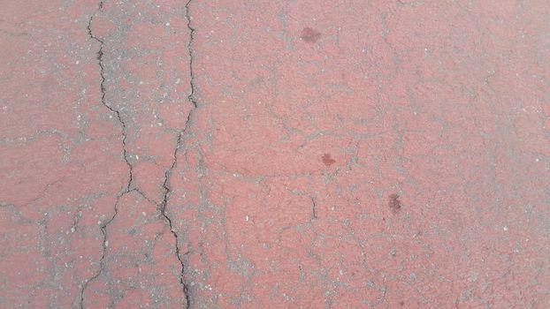 Red colored damaged road or paved pathway with crackes of different shpaes. Cracked texture with copy space for text and messages