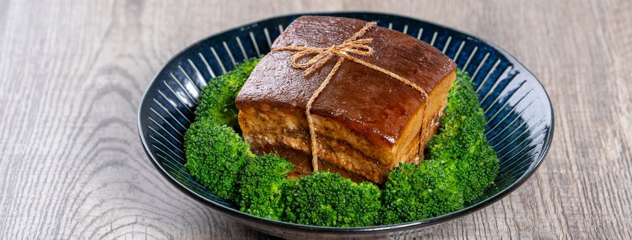 Dong Po Rou (Dongpo pork meat) in a plate with green vegetable, traditional festive food for Chinese lunar new year cuisine meal, close up.