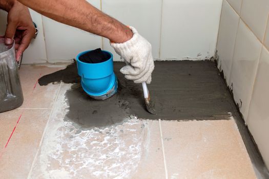 Construction workers are brushing waterproofing cement on tile floors in the bathroom.