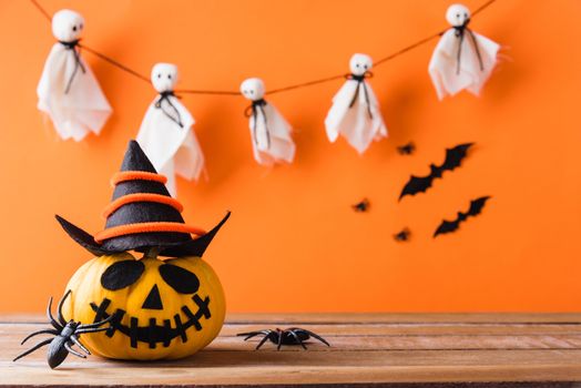 Funny Halloween day decoration party, Cute pumpkin ghost spooky jack o lantern face wear hat, black spider and bats on wooden table, studio shot isolated on an orange background, Happy holiday concept