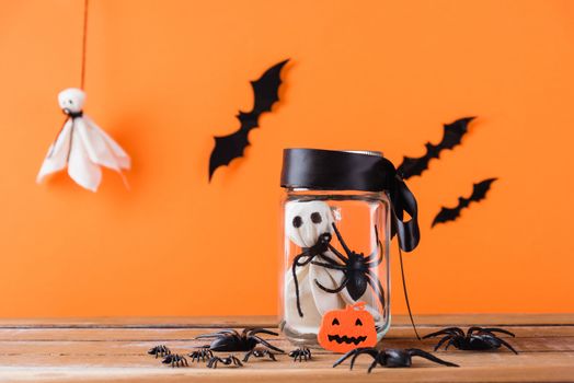 Funny Halloween day decoration party, Baby white ghost crafts scary face in jar glass on wood table, studio shot isolated on orange background have spider and bats, Happy holiday DIY concept