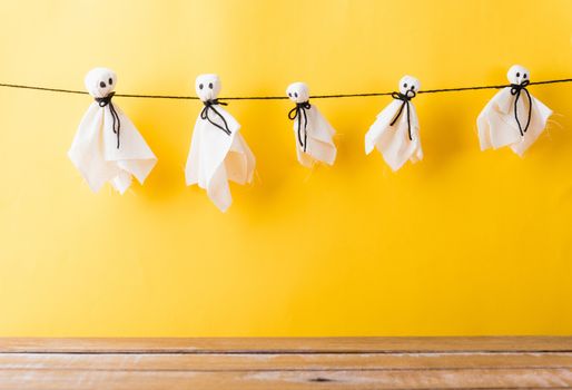 Funny Halloween day decoration party, Full body of baby cute white ghost crafts scary face hanging and wooden space, studio shot isolated on yellow background, Happy holiday DIY handicraft concept