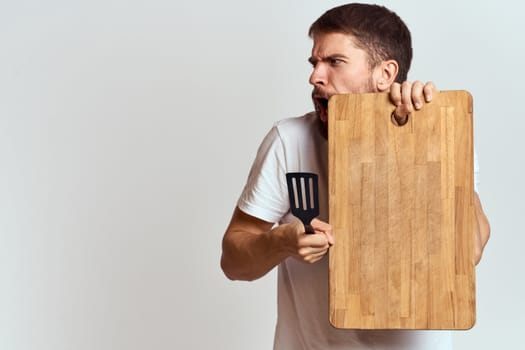 Man with a kitchen wooden board and with a shovel on a light background emotions white t-shirt model. High quality photo