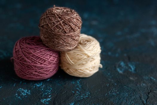 three beige pink brown Color balls skein of wool yarn for crochet and knit on dark blue texture putty concrete. Flatlay image with space for text.