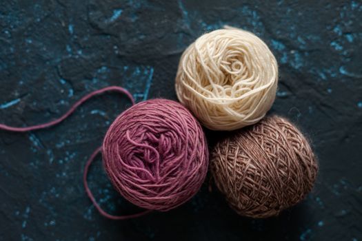 three beige pink brown Color balls skein of wool yarn for crochet and knit on dark blue texture putty concrete. Flatlay image with space for text.