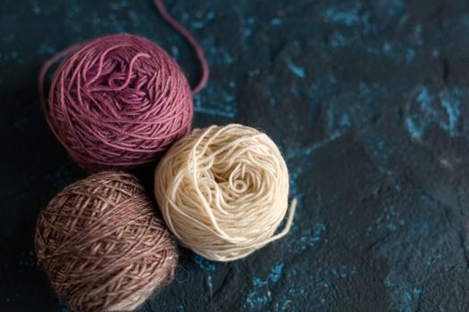 three beige pink brown Color balls skein of wool yarn for crochet and knit on dark blue texture putty concrete. Flatlay image with space for text.