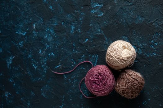 three beige pink brown Color balls skein of wool yarn for crochet and knit on dark blue texture putty concrete. Flatlay image with space for text.