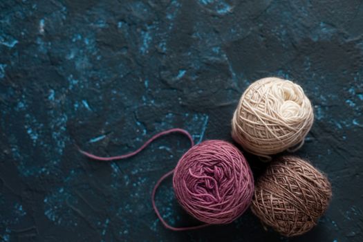 three beige pink brown Color balls skein of wool yarn for crochet and knit on dark blue texture putty concrete. Flatlay image with space for text.