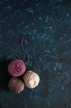 three beige pink brown Color balls skein of wool yarn for crochet and knit on dark blue texture putty concrete. Flatlay image with space for text.