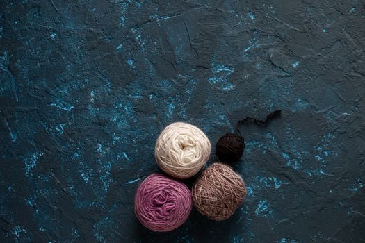 Four beige pink brown Color balls skein of wool yarn for crochet and knit on dark blue texture putty concrete. Flatlay image with space for text.