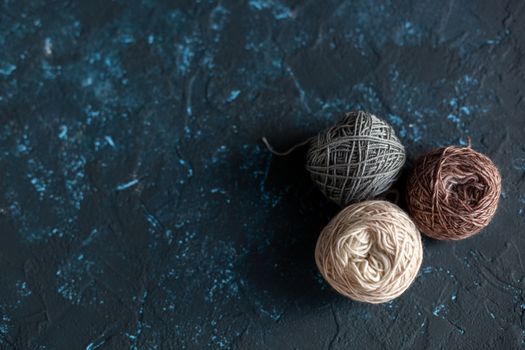 three beige gray brown Color balls skein of wool yarn for crochet and knit on dark blue texture putty concrete. Flatlay image with space for text.